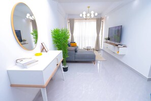 Ein modernes Wohnzimmer mit weißem Konsolentisch, einer Couch, einem gro ßen Spiegel, einem Topf mit Pflanze, einem Fernseher und einer Kristallleuchtre.