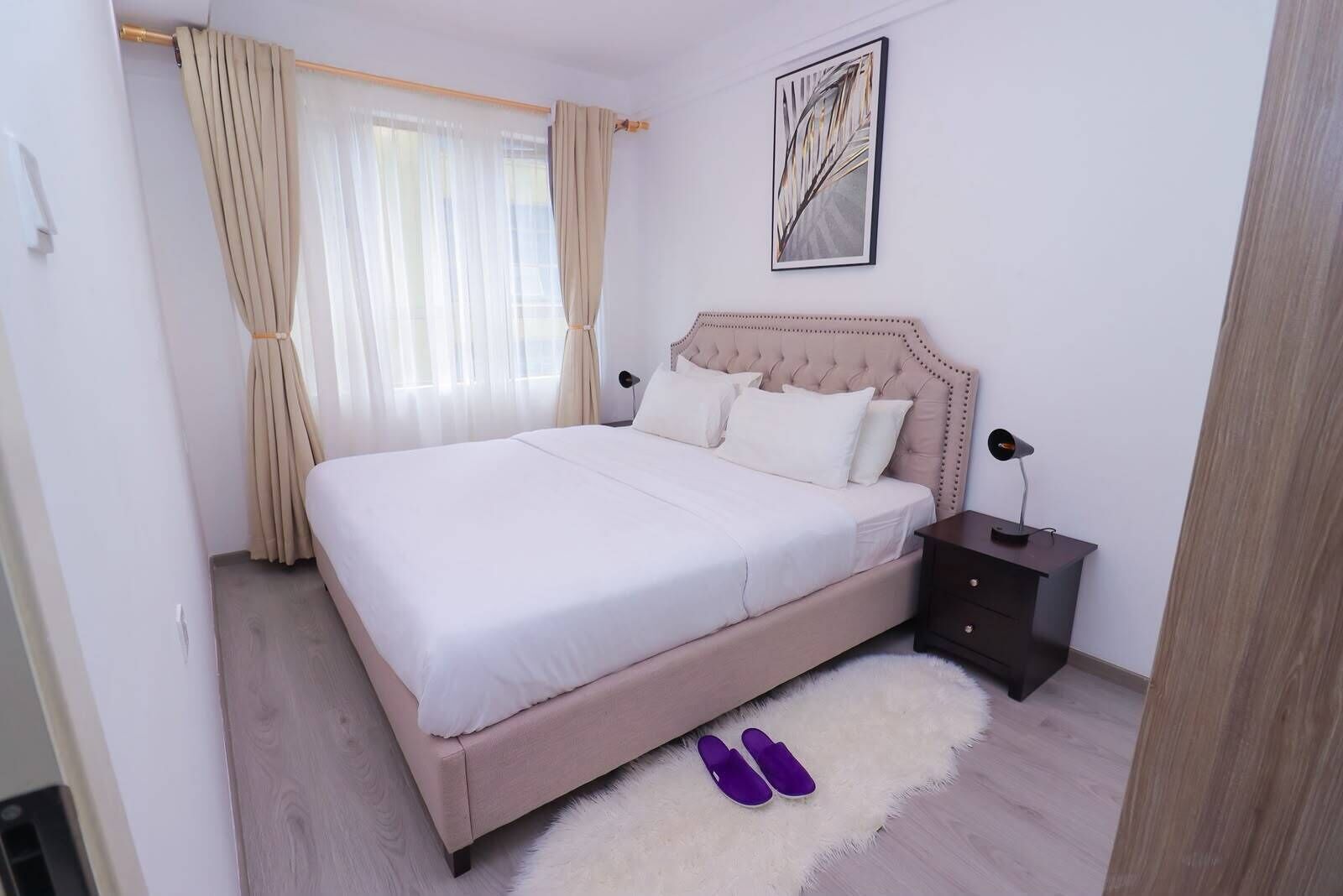A bedroom with a bed, a nightstand, a lamp, a fluffy rug, and a window with curtains.