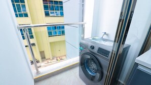 Ein kleiner Hauswirtschaftsraum mit Waschmaschine, Spüle und Fenster mit Blick auf ein Gebäude.