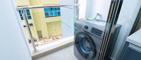 A compact laundry room with a washing machine, a small sink, and a window overlooking a building.