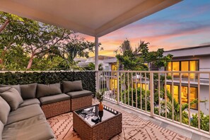 A balcony with a sofa, a coffee table, and a view of a sunset over a residential area. - Shared Pool + BBQ + Private Balcony | Walk to Las Olas | Palm Perch (Fort Lauderdale)