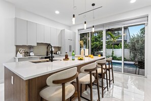 A modern kitchen with a large island, bar stools, and a view of a swimming pool. - Shared Pool + BBQ + Private Balcony | Walk to Las Olas | Palm Perch (Fort Lauderdale)
