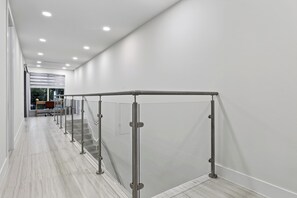 A modern hallway with a glass railing, a staircase, and a view into another room. - Shared Pool + BBQ + Private Balcony | Walk to Las Olas | Palm Perch (Fort Lauderdale)