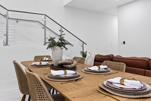 A modern dining room with a wooden table set for four, surrounded by wicker chairs. A staircase with a glass railing is visible in the background. - Shared Pool + BBQ + Private Balcony | Walk to Las Olas | Palm Perch (Fort Lauderdale)