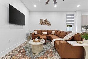 A modern living room with a brown sectional sofa, a round coffee table, and a flat-screen TV mounted on the wall. - Shared Pool + BBQ + Private Balcony | Walk to Las Olas | Palm Perch (Fort Lauderdale)