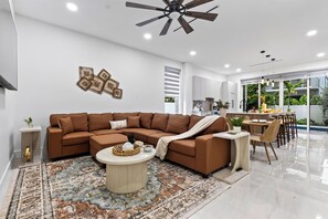 Un salon moderne avec un canapé d’angle marron, une table basse ronde et un tapis à motifs.