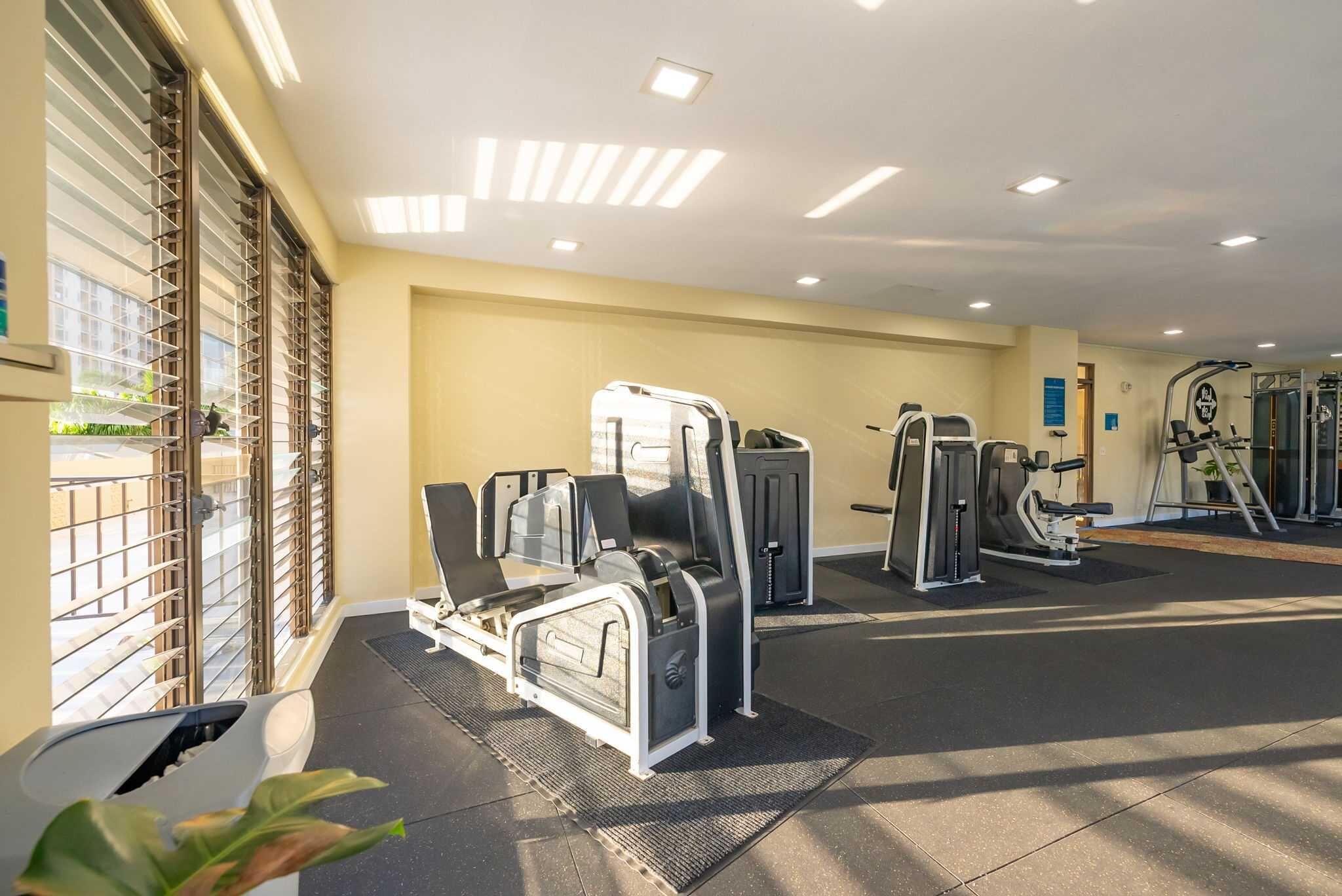 Een sportschool met trainingsapparatuur, een groot raam met zonwering en een plafond met inbouwverlichting.