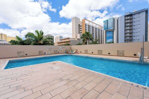 A swimming pool with a tiled deck, surrounded by a low wall with decorative patterns, and tall buildings in the background. - Royal Kuhio #1312 City Views (Honolulu)