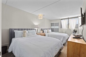 A hotel room with two beds, a bedside table, a lamp, a ceiling light, and a window with curtains. - Royal Kuhio #1312 City Views (Honolulu)
