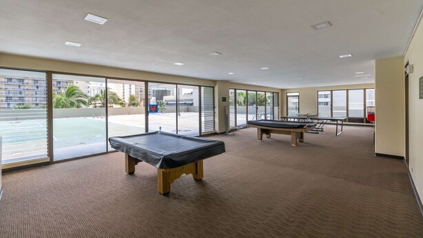 A pool table room with large windows and a view of a pool area. - Royal Kuhio #1312 City Views (Honolulu)