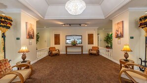 A spacious lobby with a chandelier, two armchairs, a wooden console table, and a patterned carpet. - Royal Kuhio #1312 City Views (Honolulu)
