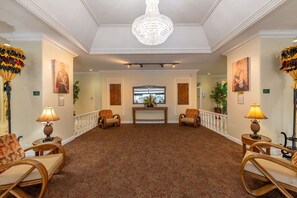 A spacious lobby with a chandelier, two armchairs, a wooden console table, and a patterned carpet. - Royal Kuhio #1312 City Views (Honolulu)