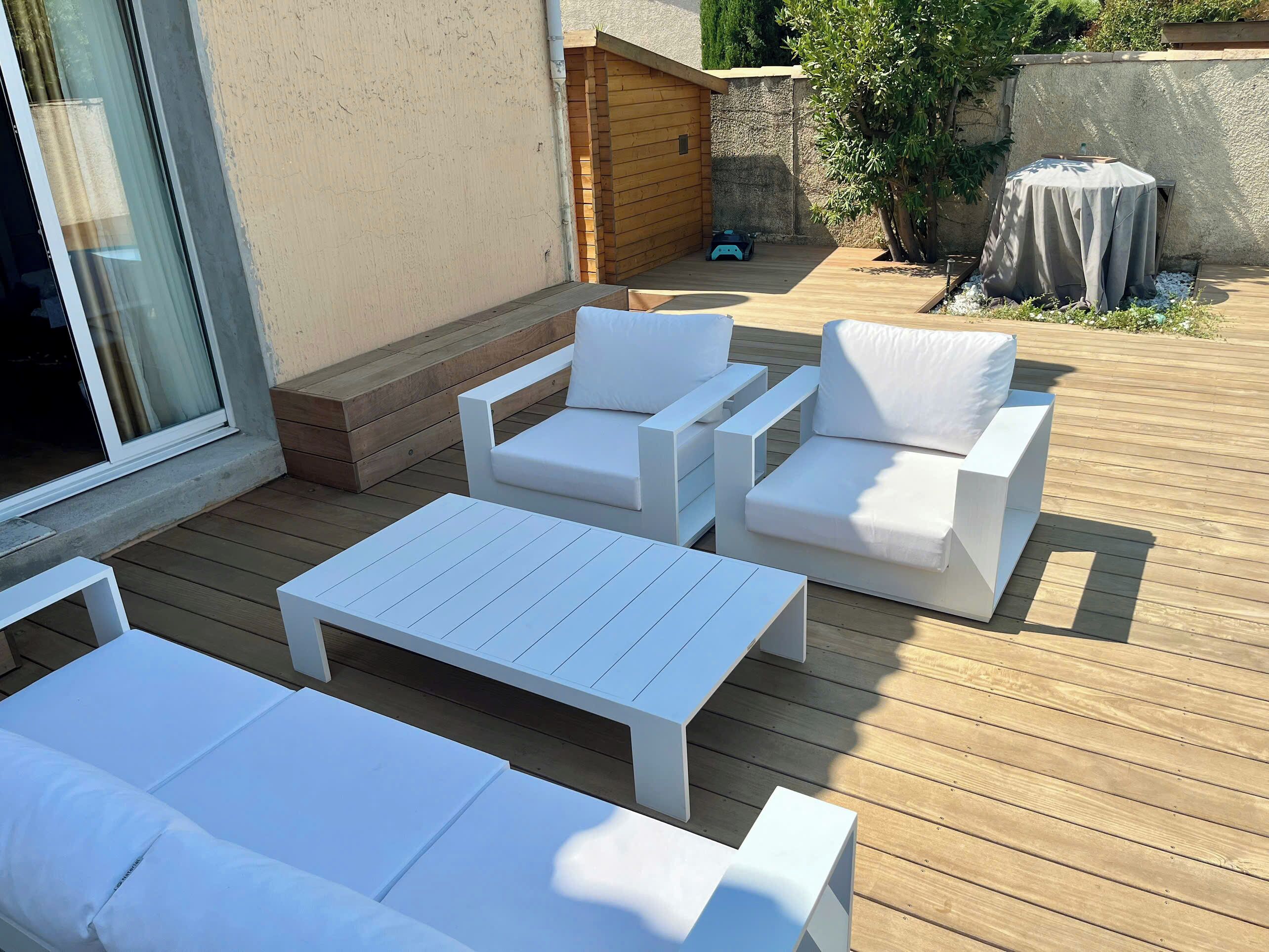 Une terrasse dotée de meubles d’extérieur blancs, notamment des canapés et une table basse.