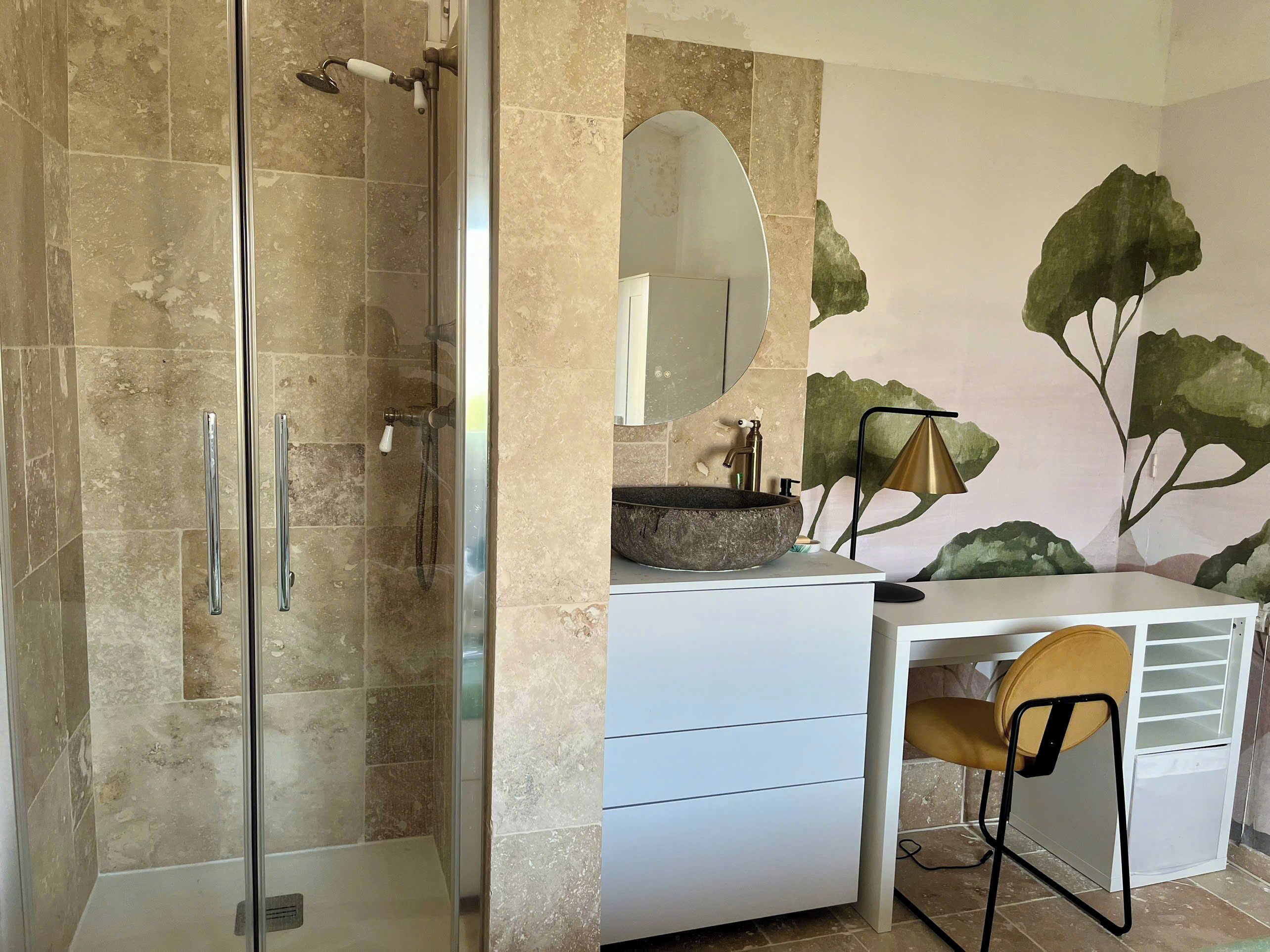 Un bagno con doccia vetrata, un mobile lavabo bianco con uno specchio grande e un affresco murale.