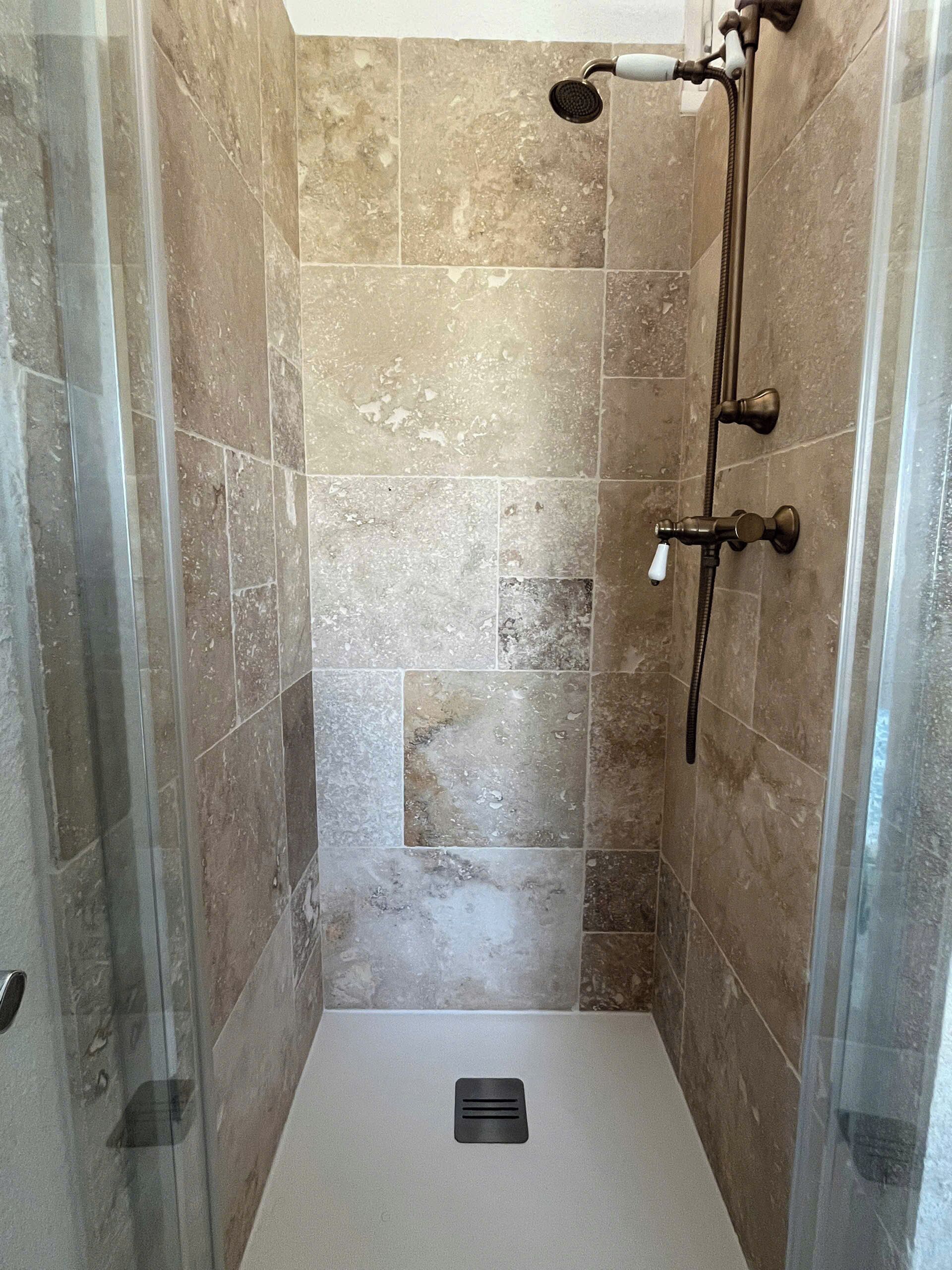 Une douche avec une porte en verre, un pommeau de douche à main et un panneau de commande fixé au mur.