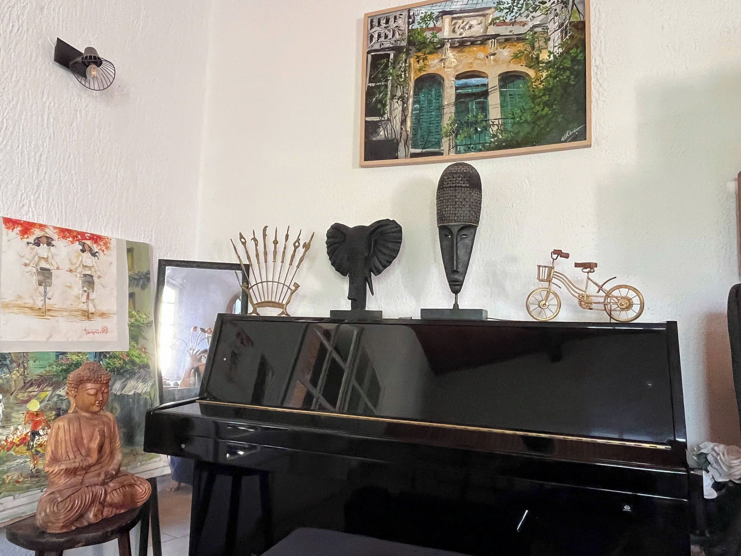Un piano orné de quelques objets décoratifs, une statue de Bouddha et un tableau encadré accroché au mur.