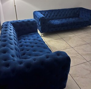 Une pièce avec deux canapés bleus recouverts de tissu et un sol carrelé.