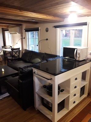 A compact kitchen with a microwave, a small countertop, and a seating area with a sofa.