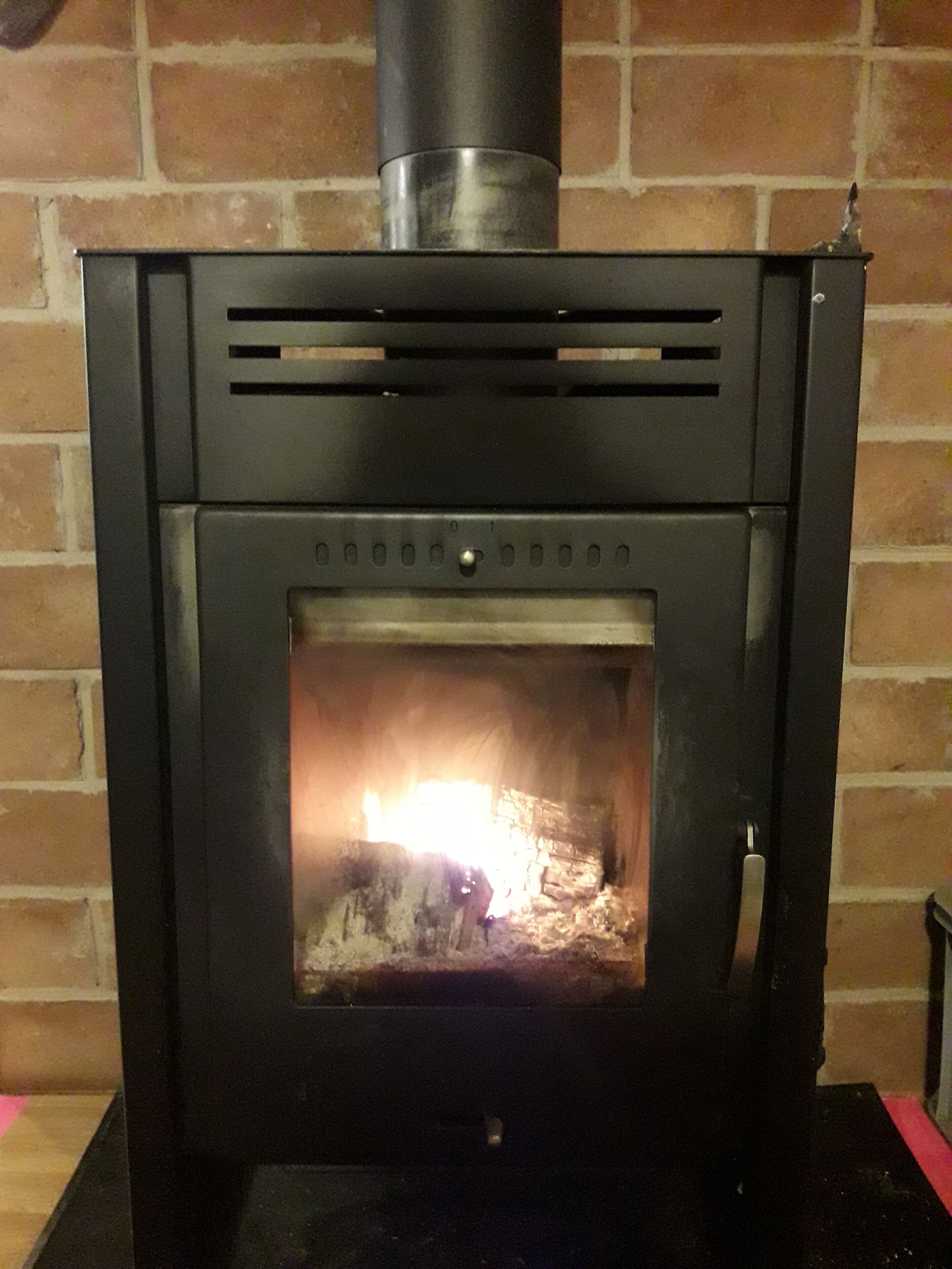 Een houtkachel met een zichtbaar vuur, geplaatst tegen een bakstenen muur.