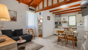A cozy living room with a sofa, a dining table with chairs, a kitchen area with a fridge, and a window with curtains. - Casa Mandulera by Villas Guide (Vodnjan)