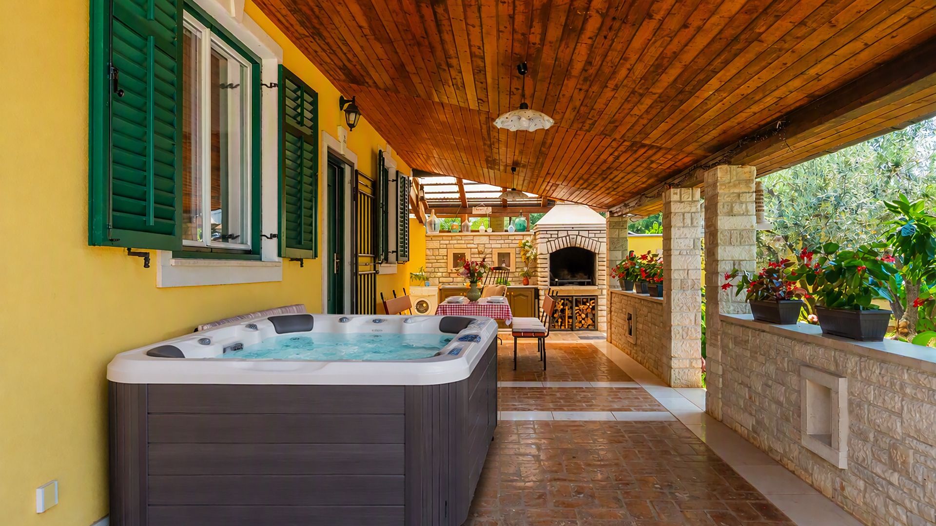A covered outdoor area with a hot tub, a stone fireplace, and a patio table.