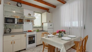 A compact kitchen with a dining area, featuring a microwave, stove, refrigerator, and a table set for two with chairs. - Casa Mandulera by Villas Guide (Vodnjan)