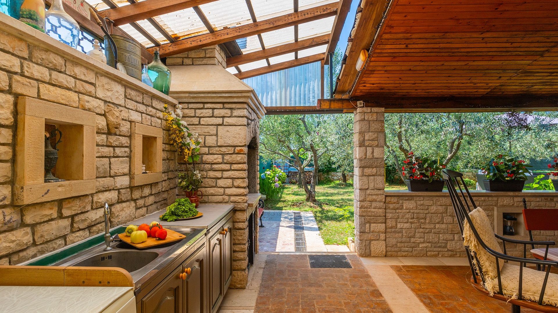 A stone kitchen with a built-in sink, a wooden countertop, and a view of a garden through a glass door.