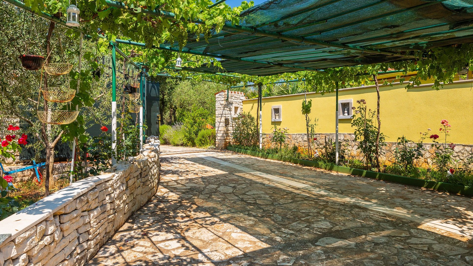 A stone-paved pathway leading to a yellow building with a stone wall on one side.