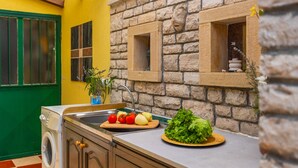A kitchen with a stone wall, a sink, a cutting board with vegetables, and a washing machine. - Casa Mandulera by Villas Guide (Vodnjan)