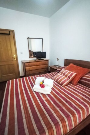 Ein Schlafzimmer mit einem Bett, einer Holzkommode, einem Schreibtisch mit Computer und einem Nachttisch mit Lampe.