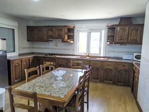 A kitchen with wooden cabinets, a granite countertop, and a dining table with chairs. - Walnut House with Private Pool by Interhome (Gondufe)