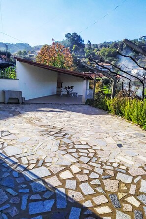 A courtyard with a stone floor, a small covered seating area, and a building with a red roof. - Walnut House with Private Pool by Interhome (Gondufe)