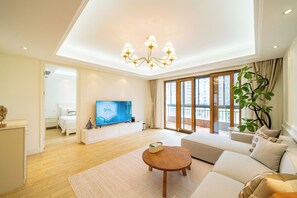 A modern living room with a flat-screen TV, a sofa, a coffee table, and a large window with a view of buildings. - Tyms Gubei International Plaza 3BR Apt (Shanghai)