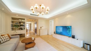 A modern living room with a large flat-screen TV, a chandelier, and a dining area with a wooden table and chairs. - Tyms Gubei International Plaza 3BR Apt (Shanghai)