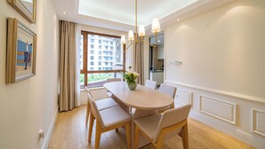 A dining area with a round table, four chairs, a vase with flowers, and a view of buildings through the window. - Tyms Gubei International Plaza 3BR Apt (Shanghai)