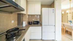 A compact kitchen with a gas stove, microwave, and a white refrigerator. - Tyms Gubei International Plaza 3BR Apt (Shanghai)