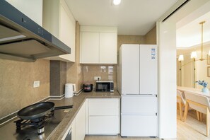 A compact kitchen with a gas stove, microwave, and a white refrigerator. - Tyms Gubei International Plaza 3BR Apt (Shanghai)