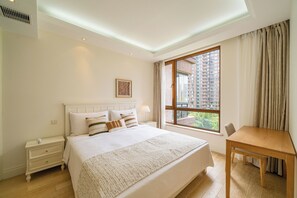 Habitación de hotel con una cama grande, una mesita de noche, una ventana con cortinas y vistas a edificios altos.