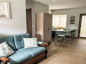 Ein Wohnzimmer mit einer Couch, einem Esstisch mit Stühlen und einer Küche im Hintergrund.