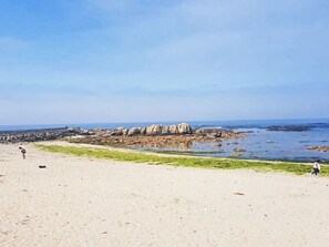 Ein Strand mit einer Felsformation, einem Steg und ruhigem Wasser.