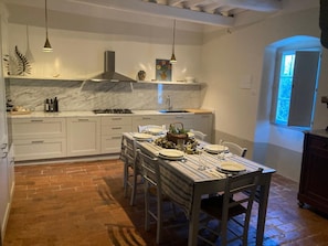 Een keuken met witte kastjes, een marmeren aanrechtblad, een gasfornuis, en een eettafel gedekt voor vier personen.