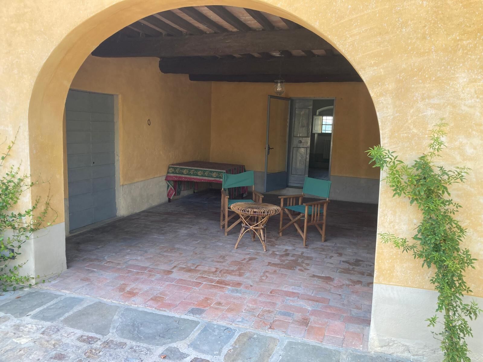 Eine überdachte Terrasse mit Tisch, Stühlen, einer Tür und einer Pflanze.