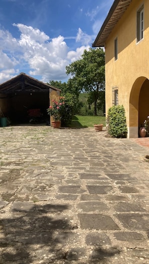 A courtyard with stone paving, a building with an arched entrance, and a garden with potted plants. - A charming 19th-century Tuscan farmhouse nestled among the vineyards of Chianti Fiorentino (San Casciano in Val di Pesa)