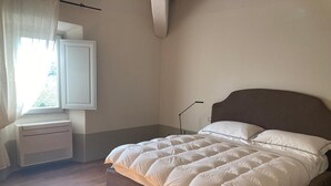Un dormitori amb un llit, una finestra amb cortines, una taula de nit i una làmpada penjada a la paret.