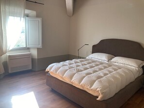 A bedroom with a bed, a window with curtains, a bedside table, and a wall-mounted light. - A charming 19th-century Tuscan farmhouse nestled among the vineyards of Chianti Fiorentino (San Casciano in Val di Pesa)