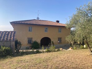 A two-story building with a tiled roof, a central archway entrance, and a small antenna on the roof. - A charming 19th-century Tuscan farmhouse nestled among the vineyards of Chianti Fiorentino (San Casciano in Val di Pesa)