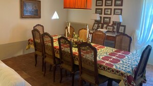Zona de menjador amb una taula preparada per a sis, amb cadires de vimetla, un mantell estampat i una làmpada taronja penjant.