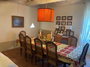 A dining area with a table set for six, surrounded by wicker chairs, a patterned tablecloth, and a hanging orange lamp. - A charming 19th-century Tuscan farmhouse nestled among the vineyards of Chianti Fiorentino (San Casciano in Val di Pesa)