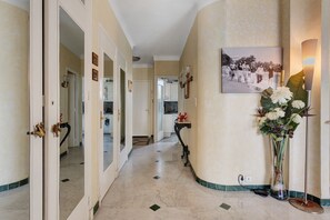 A hallway with a marble floor, a framed photograph on the wall, and a vase with flowers.