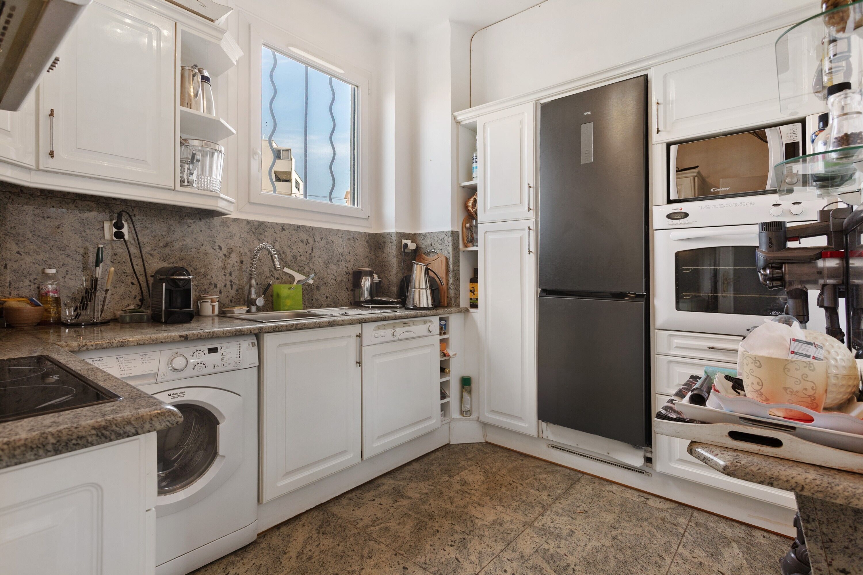 A kitchen with white cabinets, a stainless steel refrigerator, a built-in oven, and a washing machine.